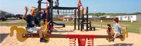 Niños jugando en un balancín y un área de juegos en Camping Jagtveld, parque vacacional en Holanda Meridional, Países Bajos.