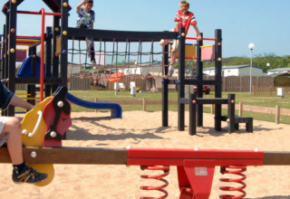 Niños jugando en un balancín y un área de juegos en Camping Jagtveld, parque vacacional en Holanda Meridional, Países Bajos.