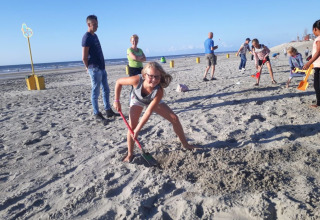 Kinderen en volwassenen graven en spelen op het strand bij Camping Jagtveld in Zuid-Holland, Nederland.