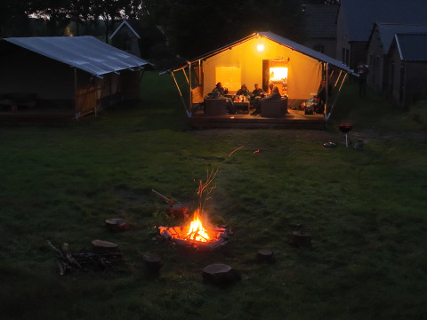 Kampvuur op grasveld bij sfeervol verlichte safaritent in vakantiepark Mooirust, Utrecht, Nederland.