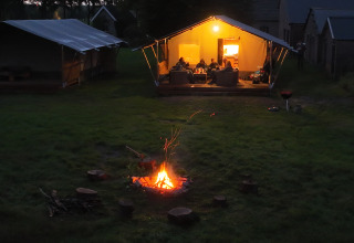 Kampvuur op grasveld bij sfeervol verlichte safaritent in vakantiepark Mooirust, Utrecht, Nederland.
