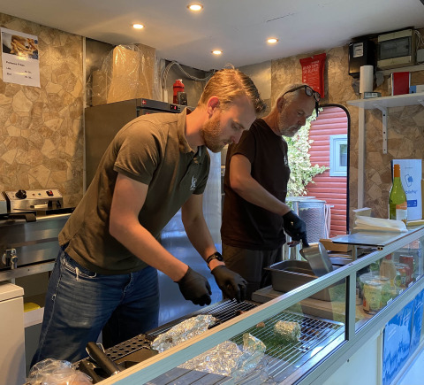 Twee mannen bereiden eten in een gezellige campingkeuken bij Tolne Camping in Noord-Jutland, Denemarken.
