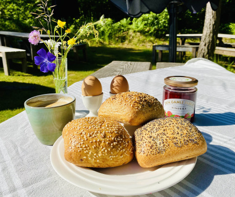 Ontbijt op Tolne Camping: verse broodjes, gekookte eieren, koffie, confituur en bloemen op tafel.