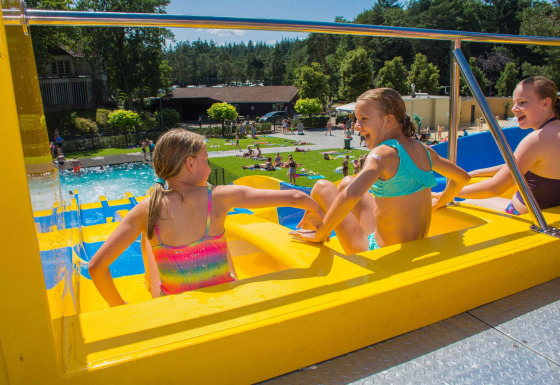 Kinderen in badkleding lachen samen op een gele waterglijbaan bij Camping Samoza in Gelderland, Nederland.