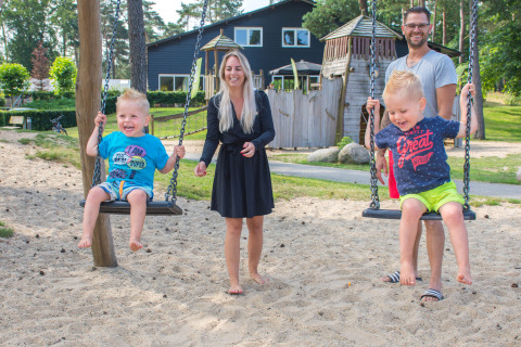 Gezin lacht en speelt op schommels bij Camping Samoza, een vakantiepark in Gelderland, Nederland.