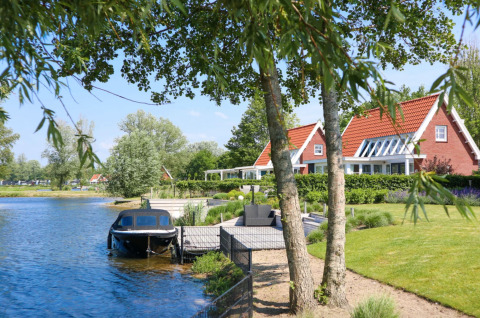 Vakantiehuisjes met rode daken en terras aan het water in vakantiedorp Bad Hoophuizen, Gelderland.