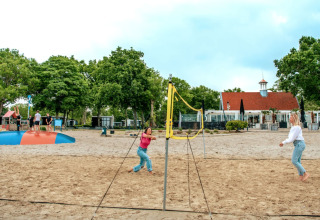 Twee vrouwen spelen beachvolleybal op het zand met vakantiepark Bad Hoophuizen op de achtergrond in Gelderland.