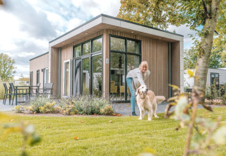 Vrouw met hond op grasveld bij modern vakantiehuisje in Bad Hoophuizen, Gelderland, Nederland.