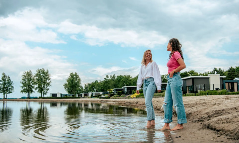 Twee vrouwen wandelen op blote voeten aan het water bij vakantiepark Bad Hoophuizen in Gelderland, Nederland.