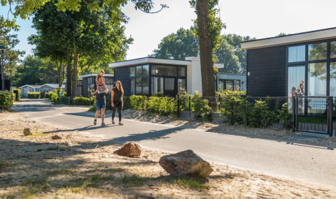 Gezin wandelt door een vakantiepark in Gelderland, Nederland, met moderne huisjes en veel groen.