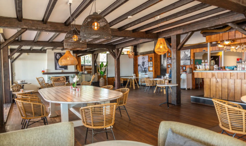 Gezellige eetruimte in Bad Hoophuizen vakantiepark, Gelderland, met houten interieur en rotanstoelen.