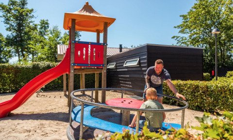Man duwt kind op een draaimolen bij een speeltuin met glijbaan in vakantiepark Bad Hoophuizen, Gelderland.