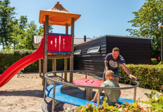 Man duwt kind op een draaimolen bij een speeltuin met glijbaan in vakantiepark Bad Hoophuizen, Gelderland.