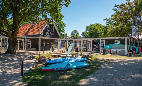 Zonnige dag bij Bad Hoophuizen vakantiepark in Gelderland, Nederland, met surfplanken en gezellige huisjes.