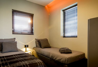 Moderne lodgeværelse på Modus i Bad Hoophuizen, Holland, med to enkeltsenge, vinduer og natbord.