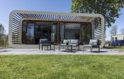Moderne Modus-lodge in Bad Hoophuizen, Nederland, met terras, buitenzitje en grasveld ervoor.