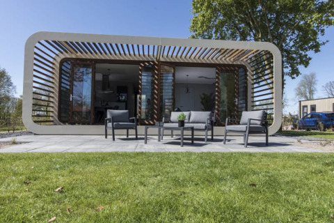 Moderne Modus-lodge in Bad Hoophuizen, Nederland, met terras, buitenzitje en grasveld ervoor.