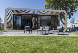 Moderne Modus-lodge in Bad Hoophuizen, Nederland, met terras, buitenzitje en grasveld ervoor.