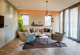 Moderne lounge in Modus-lodge bij Bad Hoophuizen, Nederland, met stijlvolle zitplaatsen en hoge ramen.