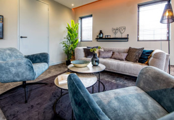 Moderne stue med blå stole, beige sofa og grøn plante på Modus-lodgen i Bad Hoophuizen, Holland.