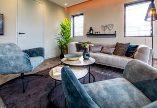 Moderne stue med blå stole, beige sofa og grøn plante på Modus-lodgen i Bad Hoophuizen, Holland.