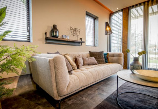 Soggiorno moderno di un lodge Modus a Bad Hoophuizen, Paesi Bassi, con grandi finestre e arredi eleganti.