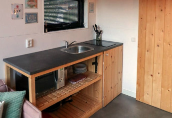 Compacte kitchenette met spoelbak, microgolfoven en houten kasten in Tiny House te Bad Hoophuizen, Nederland.