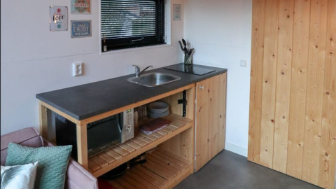 Compacte kitchenette met spoelbak, microgolfoven en houten kasten in Tiny House te Bad Hoophuizen, Nederland.