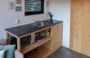 Compacte kitchenette met spoelbak, microgolfoven en houten kasten in Tiny House te Bad Hoophuizen, Nederland.