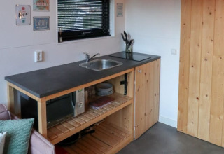 Compacte kitchenette met spoelbak, microgolfoven en houten kasten in Tiny House te Bad Hoophuizen, Nederland.