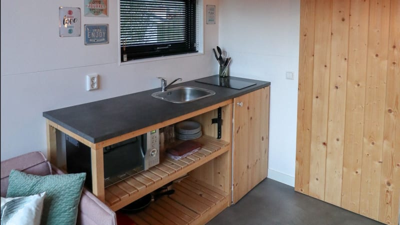 Pequeña cocina con fregadero, microondas y gabinetes de madera en Tiny House de Bad Hoophuizen, Países Bajos.