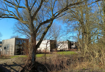 Moderne Tiny House-lodge ved Bad Hoophuizen i Holland, omringet af træer og blå himmel.