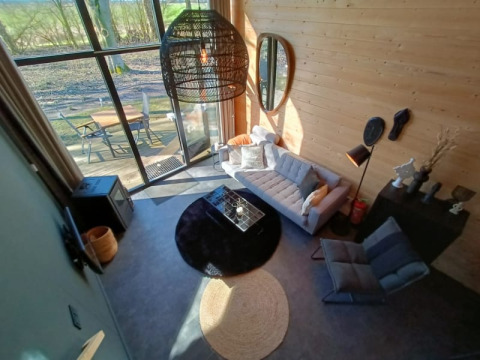 Lichte glamping woonkamer met grote ramen, designzetel en buitenterras met zicht op de natuur.