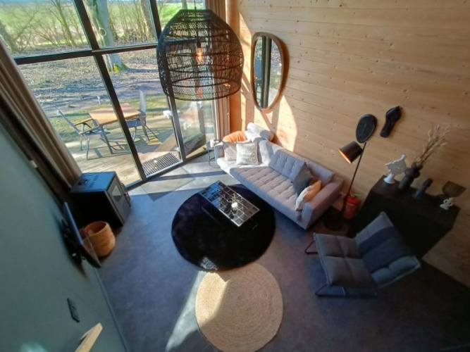 Sala de estar de glamping acogedora con grandes ventanales, sofá moderno y terraza exterior junto a la naturaleza.