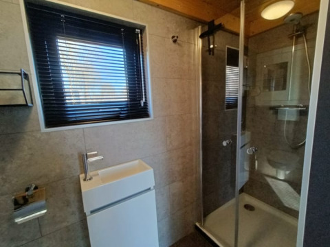 Moderne glampingbadkamer met glazen douche, wastafel en raam met jaloezieën.