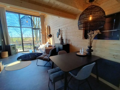 Luminoso espacio de glamping con paredes de madera, zona de comedor moderna y gran ventana al exterior.