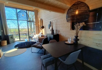 Lichte glamping-accommodatie met houten wanden, moderne eethoek en groot raam met uitzicht naar buiten.