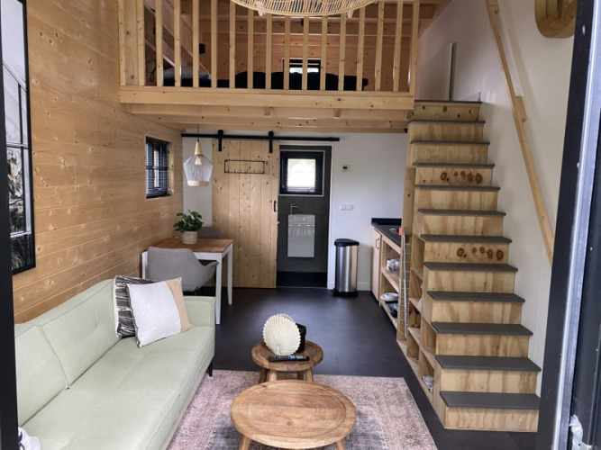 Alojamiento de glamping moderno con altillo, escalera de madera, sofá y área de comedor pequeña.