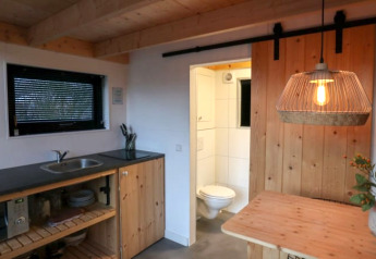 Compacte keuken en houten interieur met inkijk naar badkamer en sfeerverlichting in Tiny House, Nederland.