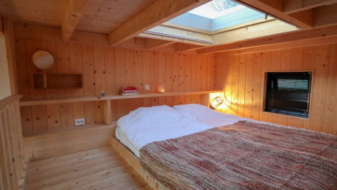 Acogedor dormitorio de madera con tragaluz en Tiny House en Bad Hoophuizen, Países Bajos, con gran cama.