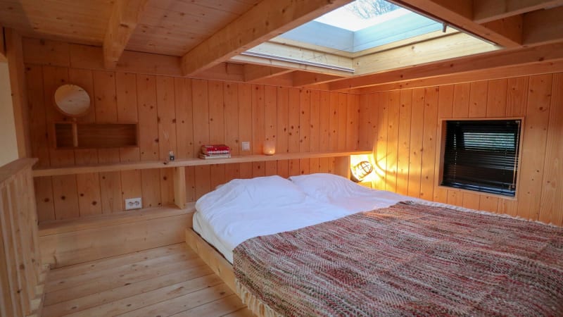 Acogedor dormitorio de madera con tragaluz en Tiny House en Bad Hoophuizen, Países Bajos, con gran cama.