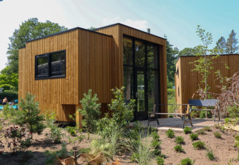 Moderne houten lodge met grote ramen, een terras en tuin, omringd door bomen en groen.