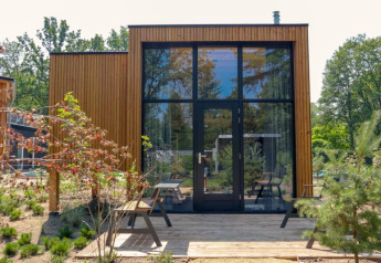 Moderne Tiny House Plus lodge bij Bad Hoophuizen, Nederland, met hoge ramen en houten gevel.