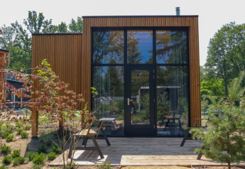 Tiny House Plus lodge bij Bad Hoophuizen, Nederland, met houten buitenkant en grote ramen.