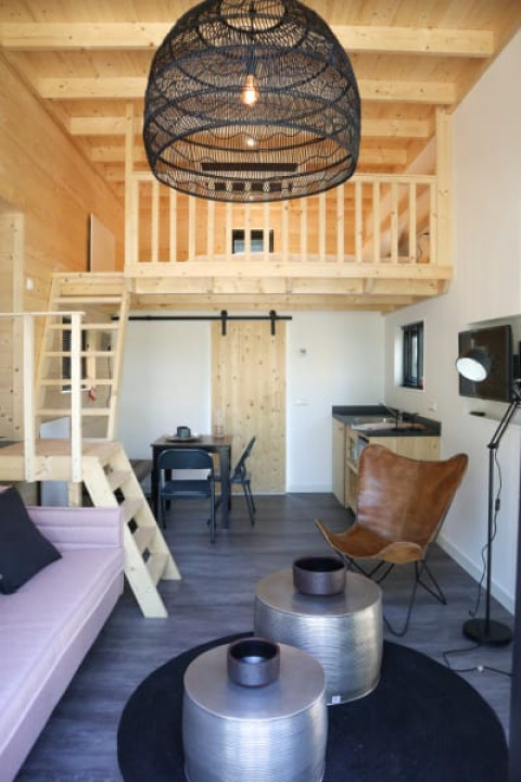 Interior de lodge moderno con altillo, decoración de madera, lámpara colgante y sala acogedora.