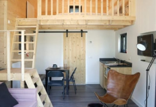 Interior de lodge moderno con altillo, decoración de madera, lámpara colgante y sala acogedora.