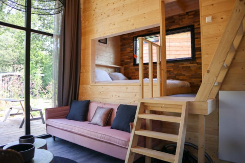 Helles Lodge-Interieur mit Holzverkleidung, rosa Sofa, großen Fenstern und erhöhtem Schlafbereich.