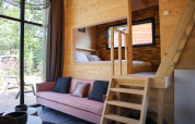 Licht lodge-interieur met houten bekleding, roze zetel, grote ramen en een knusse verhoogde slaaphoek.