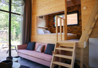 Helles Lodge-Interieur mit Holzverkleidung, rosa Sofa, großen Fenstern und erhöhtem Schlafbereich.