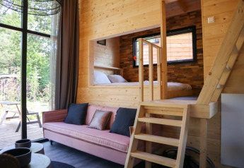Licht lodge-interieur met houten bekleding, roze zetel, grote ramen en een knusse verhoogde slaaphoek.